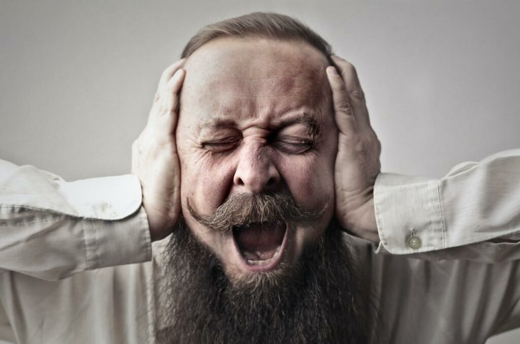 Man with a beard with hands over his ears with an open mouth,